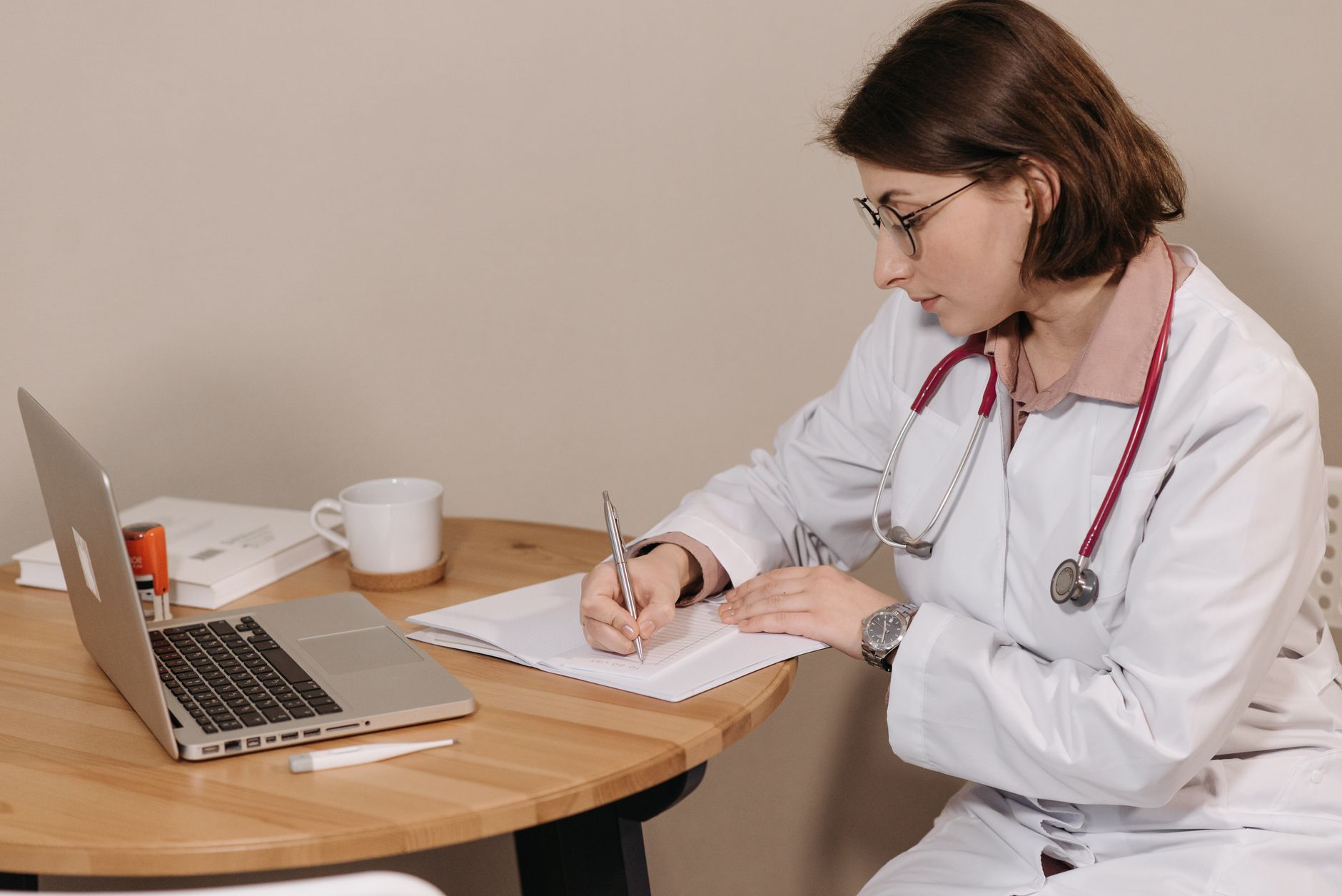 A clinic coordinator reviewing AI-powered consultation booking data on a laptop, with a WhatsApp conversation open on a smartphone beside them
