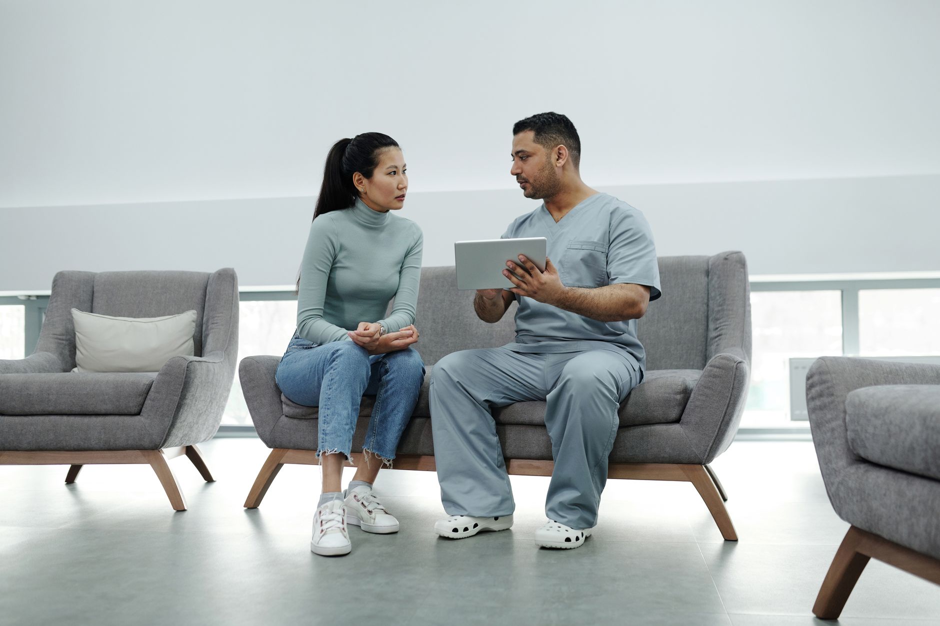 A clinic coordinator reviewing AI-powered patient follow-up messages on a laptop, with a smartphone showing a WhatsApp conversation with a UK patient enquiry